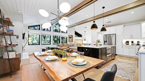 A modern kitchen with a central island, white cabinetry, and a dining area with a wooden table set for four. - Eugene Evergreen Escape by Les Chalets Stays is a fully renovated home perfect for your crew! Game room, play house, sauna, outdoor entertaining space and huge back yard. (Eugene)
