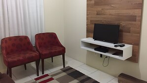 Una sala pequeña con dos sillones rojos, un mueble blanco para televisión con televisor de pantalla plana, y una pared de madera decorativa.