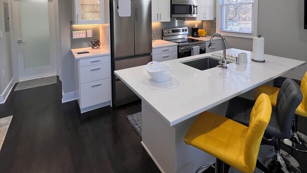 A modern kitchen with white cabinetry, stainless steel appliances, and a central island with bar stools. - Peaceful and modern retreat (Livingston)