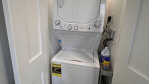 A compact, white, front-loading washer and dryer unit with a control panel, energy efficiency label, and a detergent bottle on a shelf. - Peaceful and modern retreat (Livingston)