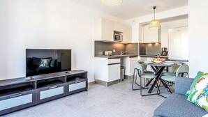A modern living room with a flat-screen TV, a dark entertainment unit, a grey sofa, and a dining area with a table and chairs. - Eden Golfe by Interhome (Cogolin)