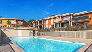 A swimming pool with a wooden deck, surrounded by apartment buildings with balconies and a clear blue sky. - Eden Golfe by Interhome (Cogolin)