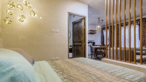 Een slaapkamer met een bed, een houten scheidingswand, een zithoek en een keuken die door een open deur zichtbaar is.