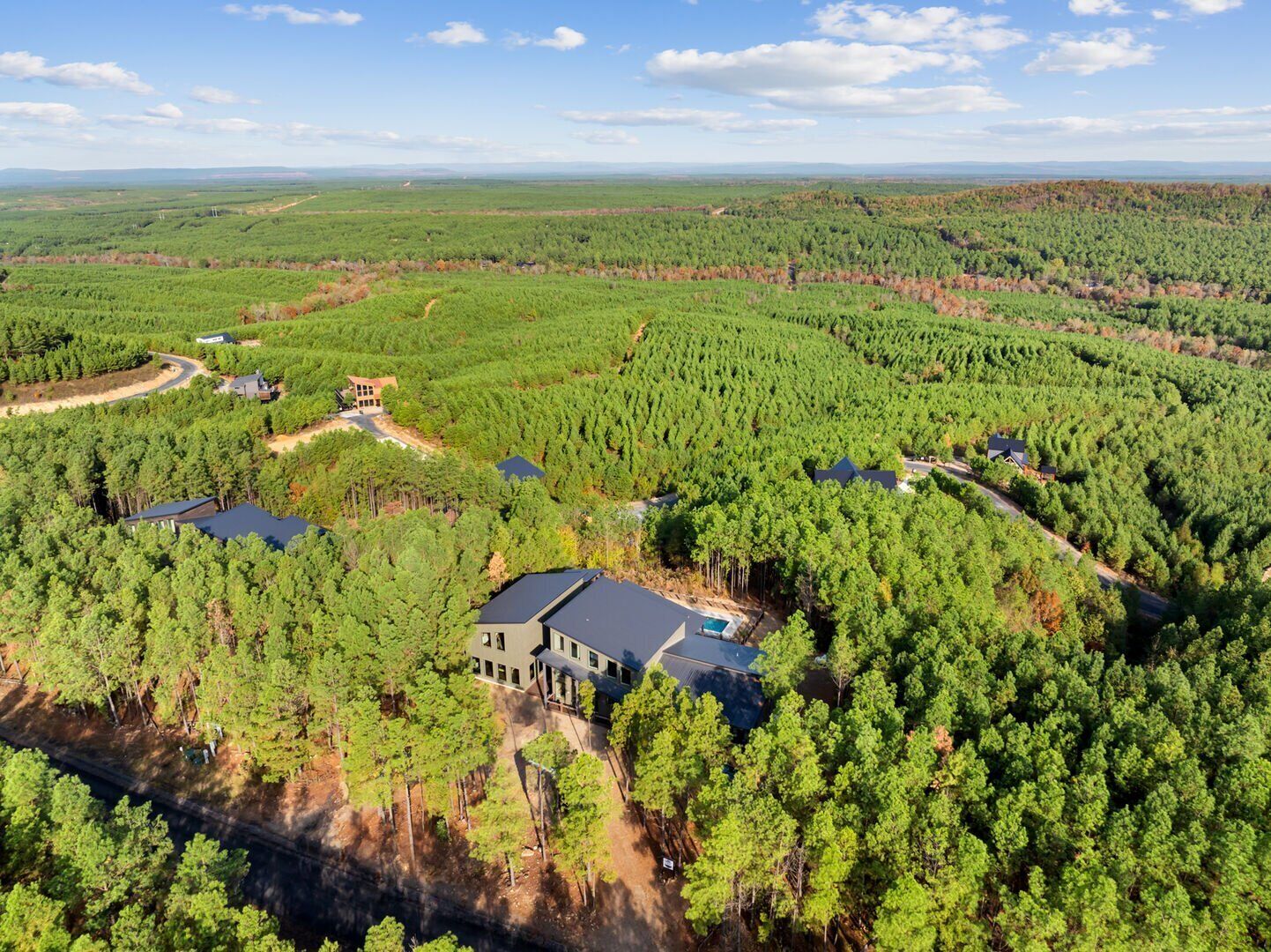 Una casa grande y moderna rodeada de un bosque frondoso, con varios accesos y una piscina visible.