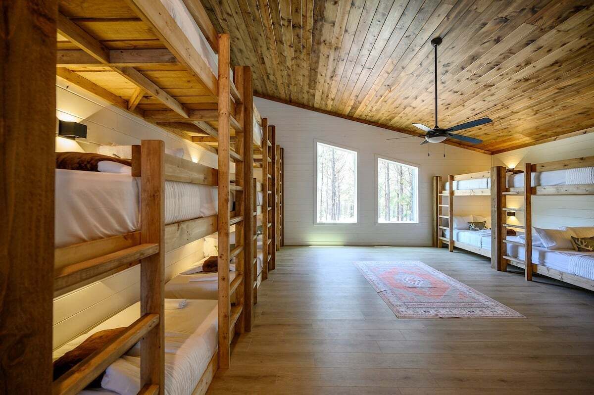 Eine Holzhütte mit einer Reihe von Etagenbetten, Holzdielen und einem Deckenventilator.