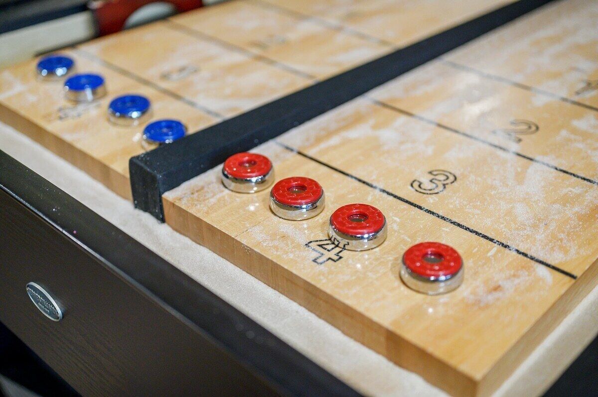 Une table de jeu de « shuffleboard » avec des zones de marquage numérotées et des palets rouges et bleus.