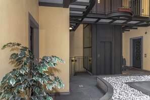 A building with a curved pathway, a potted plant, and a door with a metal gate.