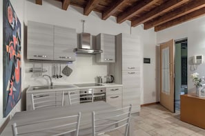 A modern kitchen with white cabinetry, a stainless steel range hood, and a dining area with a table and chairs.