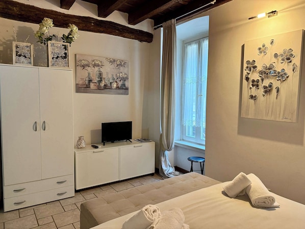 A bedroom with a bed, a TV, a wardrobe, a painting, and a window.