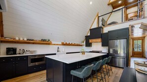 A modern kitchen with a central island, bar stools, and a stainless steel refrigerator. - Hot Tub, X Box, Fire Pit, Close 2 Town/Lake Nearby, Pets, TH (Broken Bow)