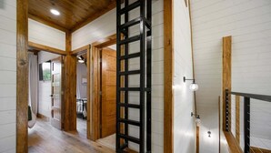 A hallway with wooden flooring and walls, a black metal gate, and a staircase with a wooden railing. - Hot Tub, X Box, Fire Pit, Close 2 Town/Lake Nearby, Pets, TH (Broken Bow)