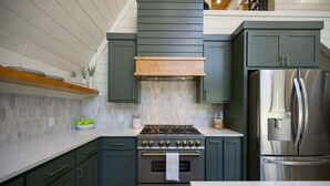 A modern kitchen with dark green cabinets, a stainless steel refrigerator, a gas stove, and a wooden ceiling.