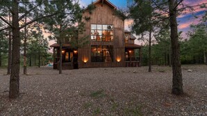 A rustic log cabin with large windows and a porch, surrounded by trees. - Mountain Views, Hot Tub, Arcade, Pets, More Than A View (Broken Bow)