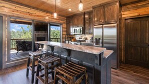 A rustic kitchen with wooden cabinets, a stainless steel refrigerator, and a large island with bar stools. - Mountain Views, Hot Tub, Arcade, Pets, More Than A View (Broken Bow)
