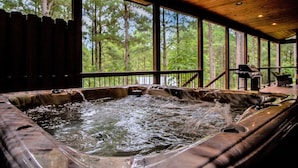 A hot tub with a wooden deck and large windows overlooking a forest. - Arcade, Play Set, Hot Tub, Pets, Makin Plans (Broken Bow)