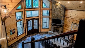 A cabin interior with a stone fireplace, large windows, and a wooden staircase. - Arcade, Play Set, Hot Tub, Pets, Makin Plans (Broken Bow)