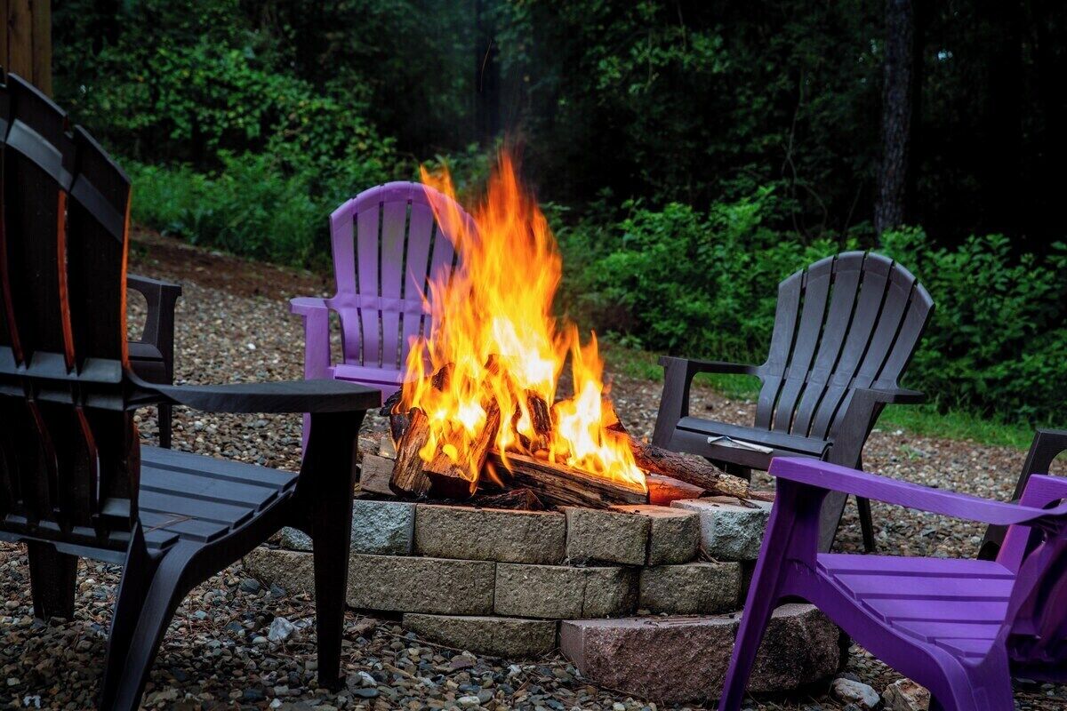 A fire pit with logs burning surrounded by outdoor chairs.