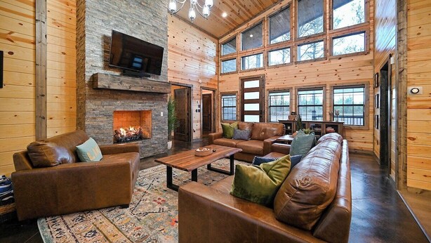 A spacious living room with a fireplace, leather sofas, and large windows. - Fenced Yard, Hot Tub, Fire pit, Swings, Pets, Surfing Sunsets (Broken Bow)
