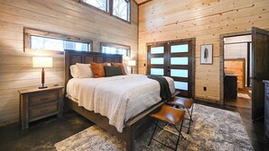 A bedroom with a wooden bed, nightstands, a bench, and a large window. - Fenced Yard, Hot Tub, Fire pit, Swings, Pets, Surfing Sunsets (Broken Bow)