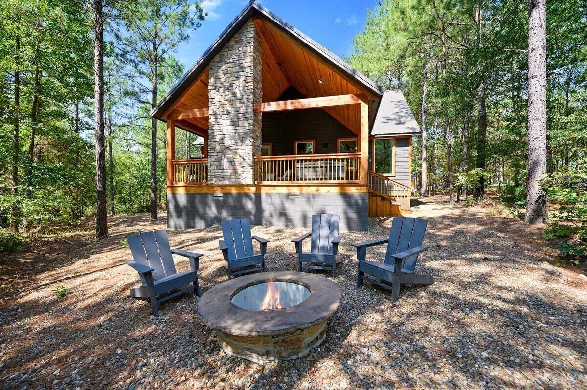 A cabin with a stone chimney, wooden deck, and outdoor seating.