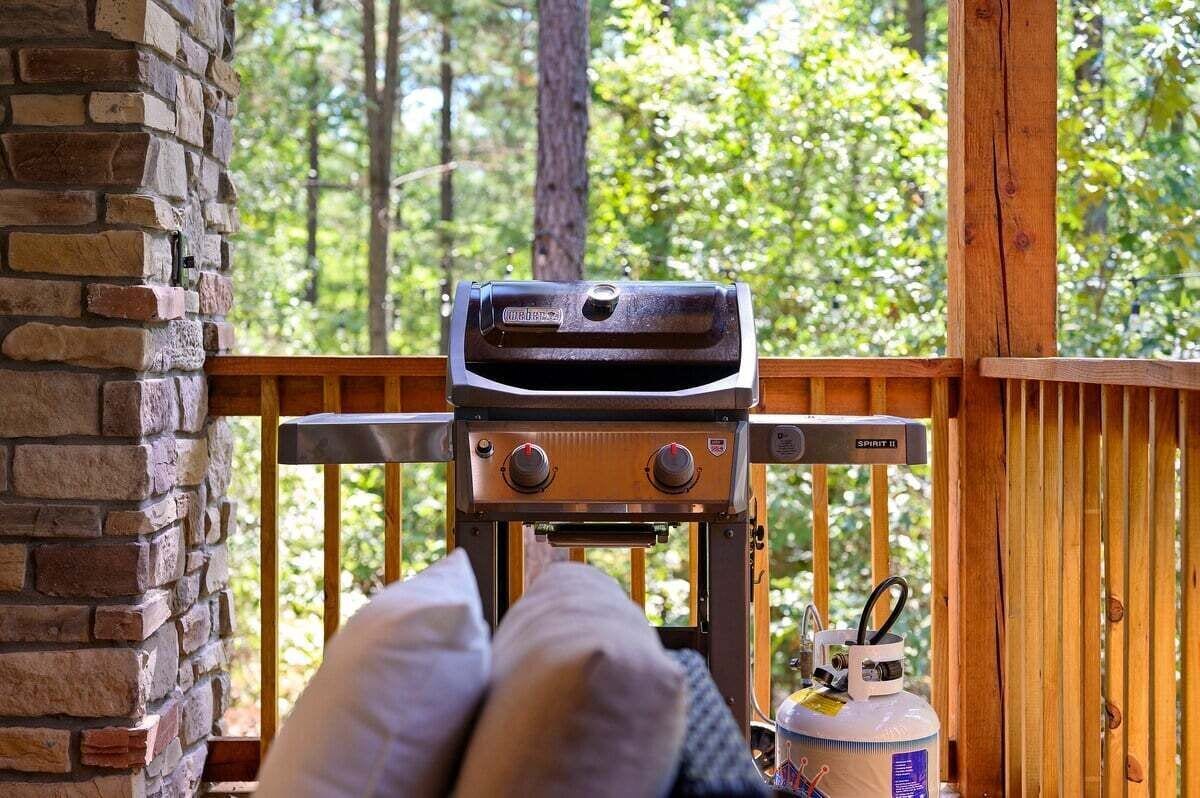 Un barbecue sur une terrasse en bois, avec un mur en briques et une rambarde en bois.