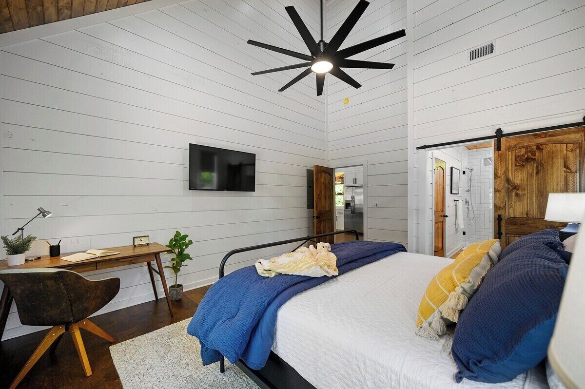 Une chambre à coucher comprenant un lit, un bureau, une chaise, un téléviseur et une porte en bois.