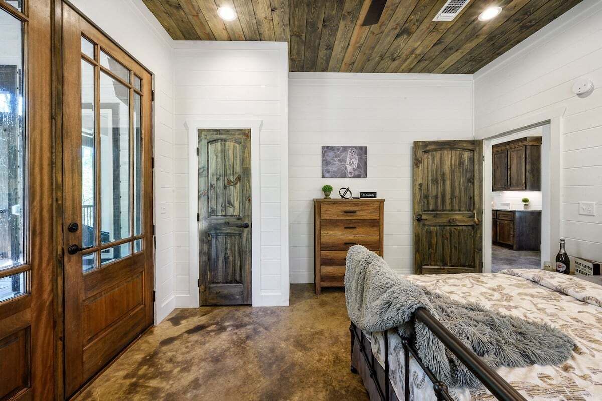 Un dormitorio con puerta de madera, cómoda, cama con manta suave y techo con vigas a la vista.