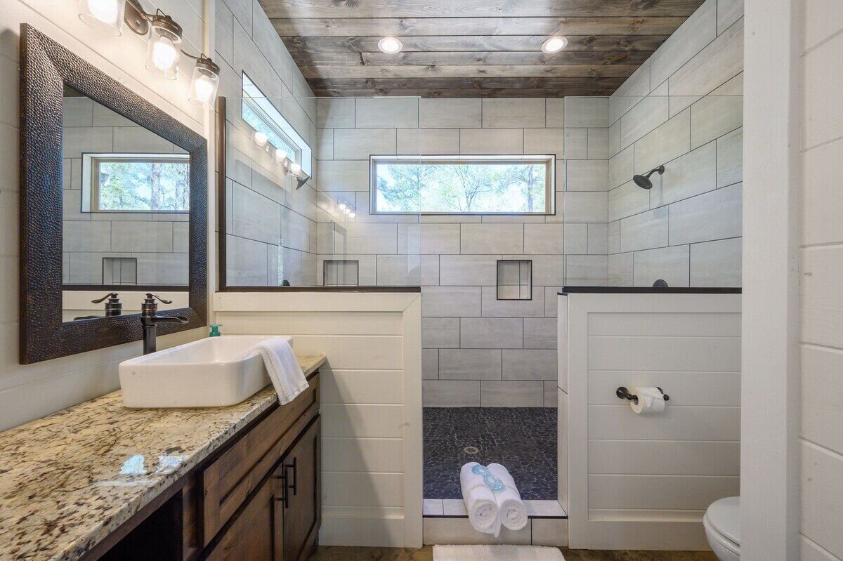 Un baño moderno con un espejo grande, un lavabo, una ducha y un inodoro.