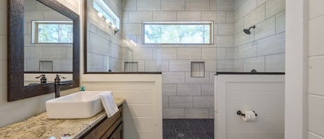 Un baño moderno con un espejo grande, un lavabo, una ducha y un inodoro.