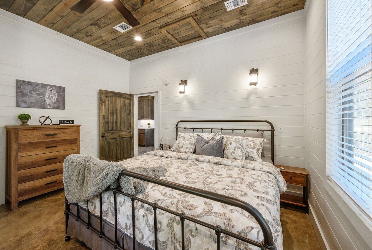 Une chambre à coucher avec un lit, une commode en bois et une porte donnant sur une autre pièce.