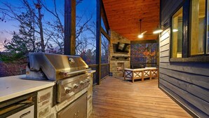 Ein Außenbereich mit einer Küche, einem Grill, einem Kamin aus Stein und einer Holzterrasse.