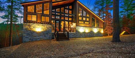 A modern log cabin with large windows, a stone foundation, and a wooden deck.