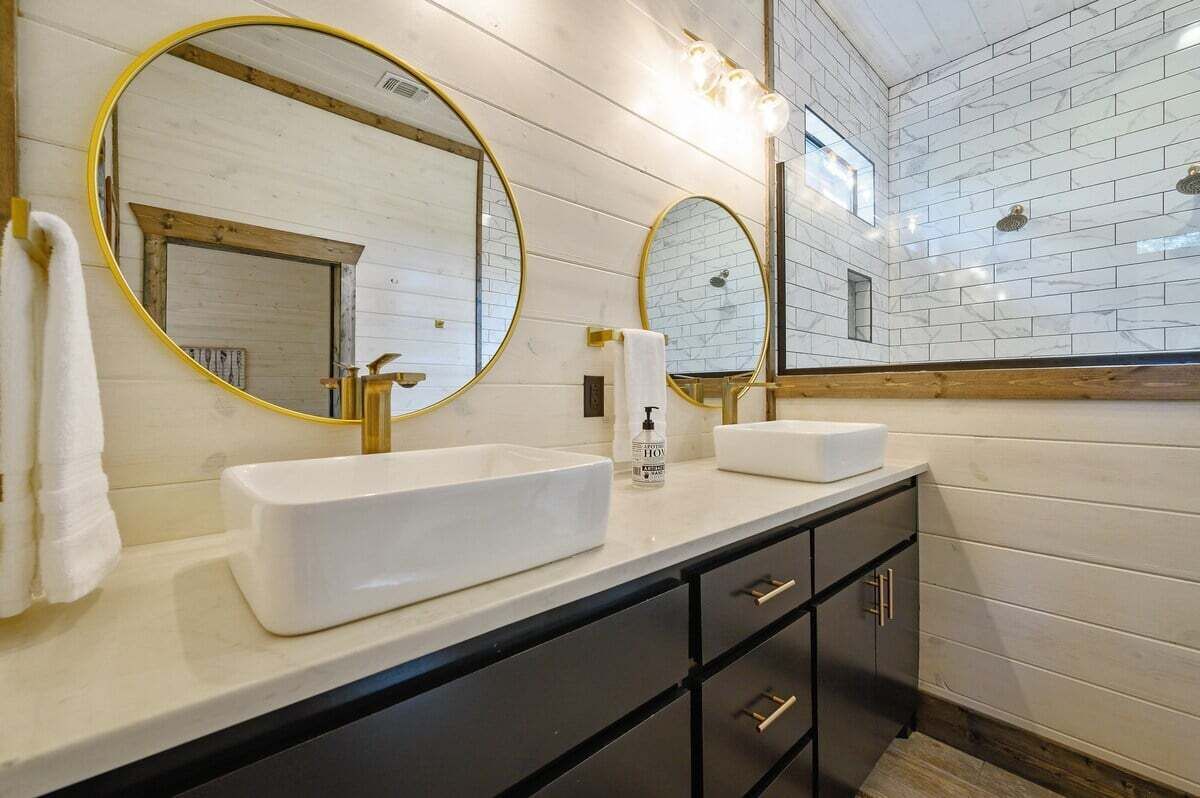 A modern bathroom with two sinks, a large mirror, and a wooden wall.