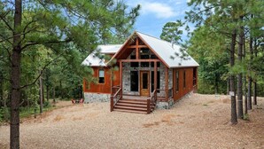 Une cabane avec des fondations en pierre, un revêtement extérieur en bois et un toit en métal, entourée de pins.