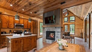 L’intérieur d’un chalet rustique, avec une cheminée en pierre, des meubles en bois et un grand îlot central doté d’un évier.