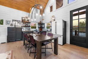 A modern kitchen with a wooden dining table, dark cabinetry, and a black refrigerator. - Hot Tub, Soaking Tub, Romantic, Close 2 Town, Pets, Vacana Pine & Bow (Broken Bow)