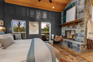 A bedroom with a large bed, a stone fireplace, and a view of the outdoors. - Hot Tub, Soaking Tub, Romantic, Close 2 Town, Pets, Vacana Pine & Bow (Broken Bow)