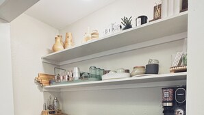 Ett kompakt kök med vita hyllor, en kaffemaskin och en pall.