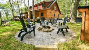 Une cabane en rondins dotée d’un patio comprenant des fauteuils Adirondack et un foyer en pierre.