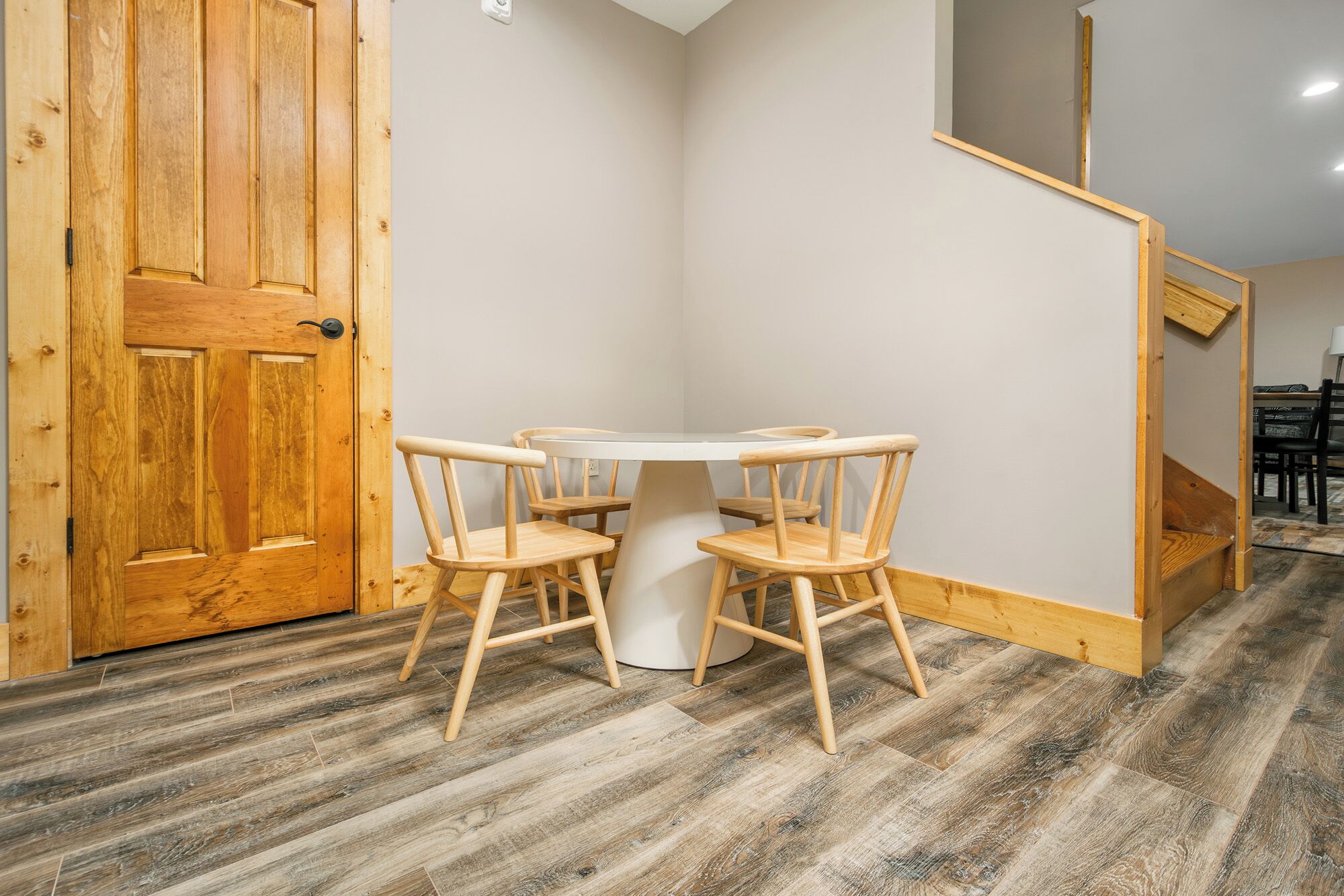 A room with a wooden door, a round table with four chairs, and a staircase in the background.