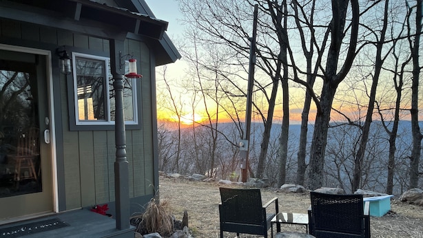 A cabin with a porch, two chairs, and a table. - COZY CABIN. One room cabin with loft. Great sunsets & river view before Spring! (Great Cacapon)