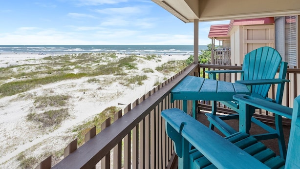 Une vue sur la plage depuis un balcon doté d’une balustrade en bois, d’une table et de deux chaises.