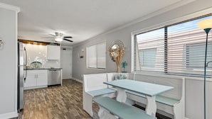Une cuisine avec des meubles blancs, une table à manger avec des bancs et un ventilateur de plafond.