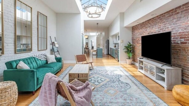 A spacious living room with a green sofa, a wooden coffee table, and a large TV on a brick wall. - The Brazo - Central Downtown Cincinnati - walk to stadiums (cincinnati)