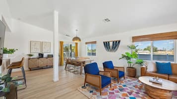 A modern living room with a wooden floor, a dining area, and a view of the sea.