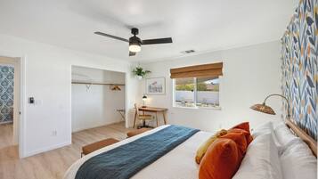 A bedroom with a bed, a desk, a chair, a window, and a ceiling fan.