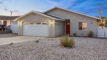 A single-story house with a garage, a red door, and a small garden with desert plants.