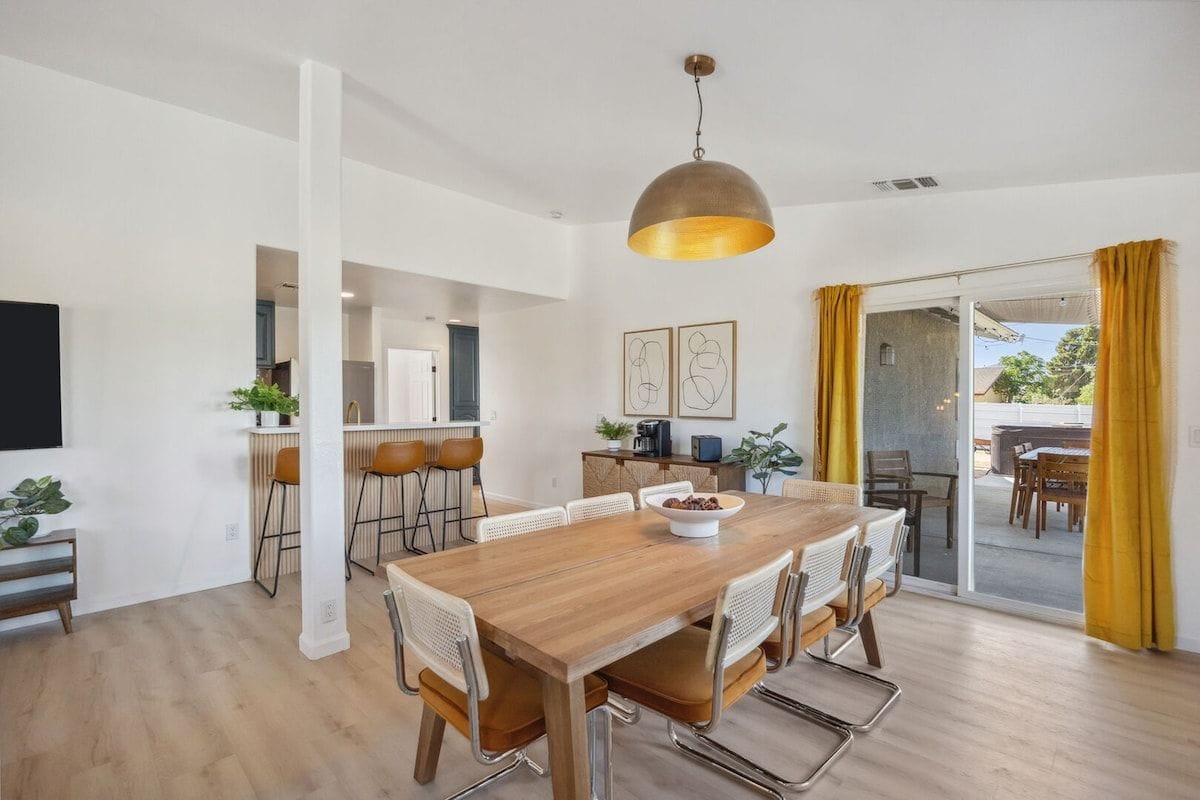 Un comedor moderno con mesa y sillas de madera, una lámpara colgante y vistas al exterior.