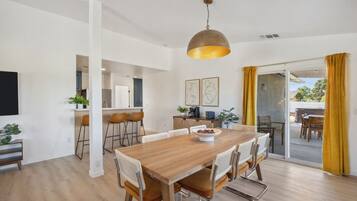 A modern dining area with a wooden table and chairs, a pendant light, and a view to the outside.