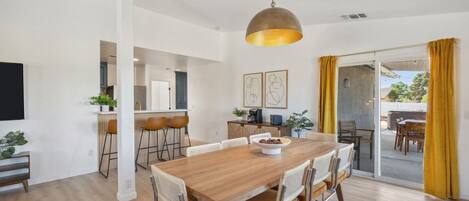 Un comedor moderno con mesa y sillas de madera, una lámpara colgante y vistas al exterior.